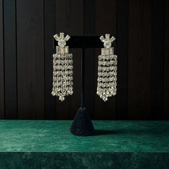 Vintage 1960s clip-on earrings with cascading clear rhinestone dangles, featuring chaton and baguette stones in a waterfall design, displayed on a black stand.