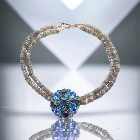 A stunning vintage Weiss crystal dome brooch in shades of blue and teal, paired with a double strand of shiny blue and gray faceted labradorite rondelles. The brooch can be worn centered, off-center, or separately, offering versatile styling. Finished with sterling silver spacers and a toggle clasp, this unique piece blends vintage charm with modern craftsmanship, signed Weiss on the back and featuring the EM tag in Etruscan alphabet for Elisabeth Michel-Meyrueix.