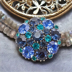 A stunning vintage Weiss crystal dome brooch in shades of blue and teal, paired with a double strand of shiny blue and gray faceted labradorite rondelles. The brooch can be worn centered, off-center, or separately, offering versatile styling. Finished with sterling silver spacers and a toggle clasp, this unique piece blends vintage charm with modern craftsmanship, signed Weiss on the back and featuring the EM tag in Etruscan alphabet for Elisabeth Michel-Meyrueix.