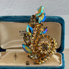 Gold‑tone vintage brooch with AB topaz, smoky, and clear rhinestones in a floral swirl shape.