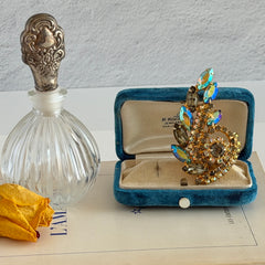 Gold‑tone vintage brooch with AB topaz, smoky, and clear rhinestones in a floral swirl shape.