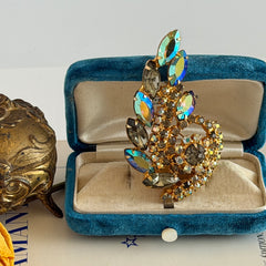 Gold‑tone vintage brooch with AB topaz, smoky, and clear rhinestones in a floral swirl shape.