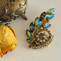 Gold‑tone vintage brooch with AB topaz, smoky, and clear rhinestones in a floral swirl shape.