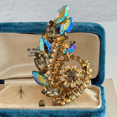 Gold‑tone vintage brooch with AB topaz, smoky, and clear rhinestones in a floral swirl shape.