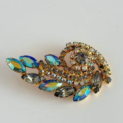 Gold‑tone vintage brooch with AB topaz, smoky, and clear rhinestones in a floral swirl shape.