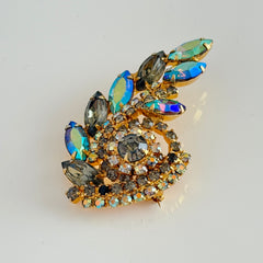 Gold‑tone vintage brooch with AB topaz, smoky, and clear rhinestones in a floral swirl shape.