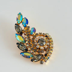 Gold‑tone vintage brooch with AB topaz, smoky, and clear rhinestones in a floral swirl shape.