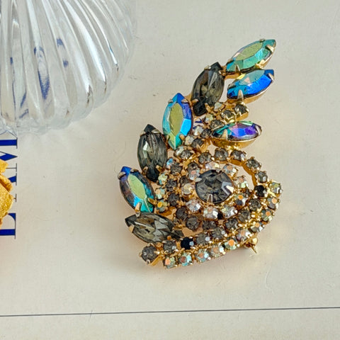 Gold‑tone vintage brooch with AB topaz, smoky, and clear rhinestones in a floral swirl shape.