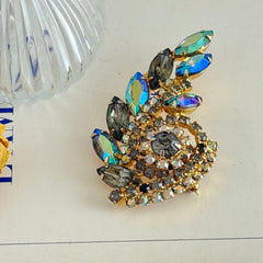 Gold‑tone vintage brooch with AB topaz, smoky, and clear rhinestones in a floral swirl shape.