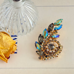 Gold‑tone vintage brooch with AB topaz, smoky, and clear rhinestones in a floral swirl shape.