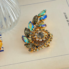 Gold‑tone vintage brooch with AB topaz, smoky, and clear rhinestones in a floral swirl shape.