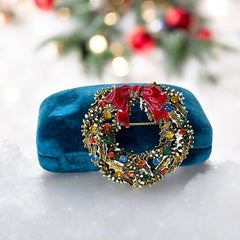 Vintage ART signed Christmas wreath brooch with red and white enamel, multicolor rhinestones, gold-tone openwork design, and red bow; mid-century holiday jewelry in very good condition.