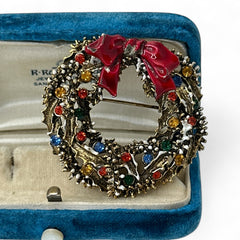 Vintage ART signed Christmas wreath brooch with red and white enamel, multicolor rhinestones, gold-tone openwork design, and red bow; mid-century holiday jewelry in very good condition.