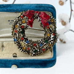Vintage ART signed Christmas wreath brooch with red and white enamel, multicolor rhinestones, gold-tone openwork design, and red bow; mid-century holiday jewelry in very good condition.