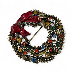 Vintage ART signed Christmas wreath brooch with red and white enamel, multicolor rhinestones, gold-tone openwork design, and red bow; mid-century holiday jewelry in very good condition.