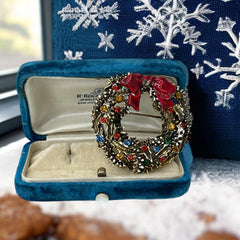 Vintage ART signed Christmas wreath brooch with red and white enamel, multicolor rhinestones, gold-tone openwork design, and red bow; mid-century holiday jewelry in very good condition.