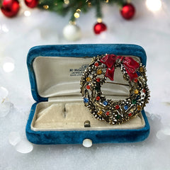Vintage ART signed Christmas wreath brooch with red and white enamel, multicolor rhinestones, gold-tone openwork design, and red bow; mid-century holiday jewelry in very good condition.