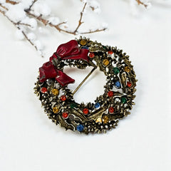 Vintage ART signed Christmas wreath brooch with red and white enamel, multicolor rhinestones, gold-tone openwork design, and red bow; mid-century holiday jewelry in very good condition.