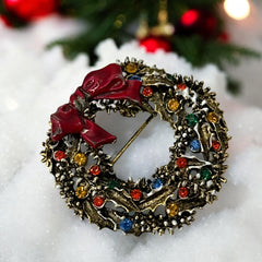 Vintage ART signed Christmas wreath brooch with red and white enamel, multicolor rhinestones, gold-tone openwork design, and red bow; mid-century holiday jewelry in very good condition.