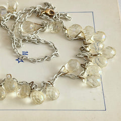 Vintage 1990s long necklace with acrylic faceted briolettes on a mixed‑metal chain, displayed with vintage props.