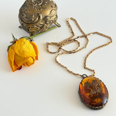Vintage brass locket pendant with a warm glass cabochon, floral detailing, and a signed Krementz gold‑plated serpentine chain.