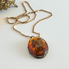 Vintage brass locket pendant with a warm glass cabochon, floral detailing, and a signed Krementz gold‑plated serpentine chain.