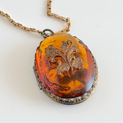 Vintage brass locket pendant with a warm glass cabochon, floral detailing, and a signed Krementz gold‑plated serpentine chain.