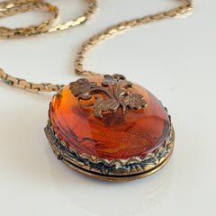 Vintage brass locket pendant with a warm glass cabochon, floral detailing, and a signed Krementz gold‑plated serpentine chain.