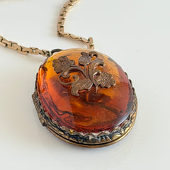 Vintage brass locket pendant with a warm glass cabochon, floral detailing, and a signed Krementz gold‑plated serpentine chain.