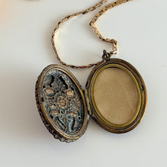 Vintage brass locket pendant with a warm glass cabochon, floral detailing, and a signed Krementz gold‑plated serpentine chain.