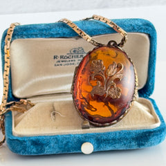 Vintage brass locket pendant with a warm glass cabochon, floral detailing, and a signed Krementz gold‑plated serpentine chain.