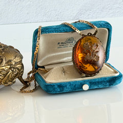 Vintage brass locket pendant with a warm glass cabochon, floral detailing, and a signed Krementz gold‑plated serpentine chain.