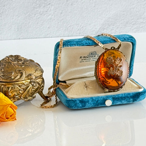 Vintage brass locket pendant with a warm glass cabochon, floral detailing, and a signed Krementz gold‑plated serpentine chain.