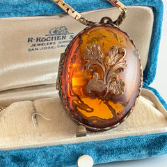 Vintage brass locket pendant with a warm glass cabochon, floral detailing, and a signed Krementz gold‑plated serpentine chain.