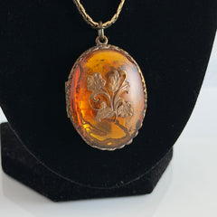 Vintage brass locket pendant with a warm glass cabochon, floral detailing, and a signed Krementz gold‑plated serpentine chain.