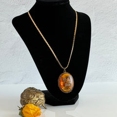 Vintage brass locket pendant with a warm glass cabochon, floral detailing, and a signed Krementz gold‑plated serpentine chain.