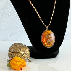 Vintage brass locket pendant with a warm glass cabochon, floral detailing, and a signed Krementz gold‑plated serpentine chain.