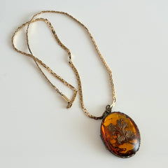 Vintage brass locket pendant with a warm glass cabochon, floral detailing, and a signed Krementz gold‑plated serpentine chain.