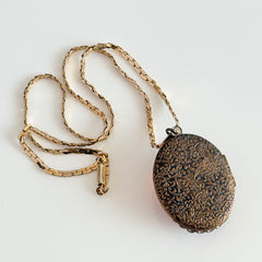 Vintage brass locket pendant with a warm glass cabochon, floral detailing, and a signed Krementz gold‑plated serpentine chain.