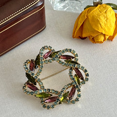 Vintage gold tone wreath brooch with amethyst, peridot, and blue rhinestones, shown in various decorative arrangements.