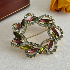 Vintage gold tone wreath brooch with amethyst, peridot, and blue rhinestones, shown in various decorative arrangements.