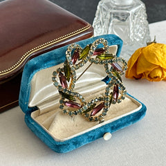 Vintage gold tone wreath brooch with amethyst, peridot, and blue rhinestones, shown in various decorative arrangements.