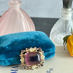Vintage gold‑tone brooch with an amethyst‑colored rhinestone, faux pearls, and white enamel flowers