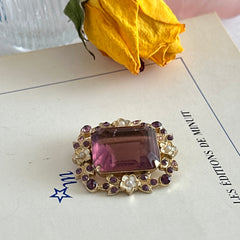 Vintage gold‑tone brooch with an amethyst‑colored rhinestone, faux pearls, and white enamel flowers