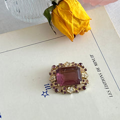 Vintage gold‑tone brooch with an amethyst‑colored rhinestone, faux pearls, and white enamel flowers