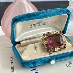 Vintage gold‑tone brooch with an amethyst‑colored rhinestone, faux pearls, and white enamel flowers