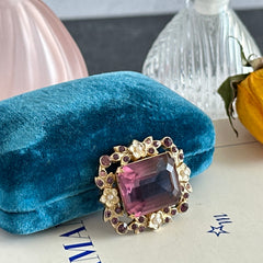 Vintage gold‑tone brooch with an amethyst‑colored rhinestone, faux pearls, and white enamel flowers