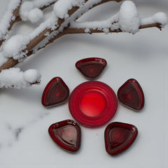 Vintage Anchor Hocking Royal Ruby relish trays arranged in a circular pattern around a coordinating red glass plate. The translucent ruby red glass glows with depth and symmetry, showcasing the sculptural triangular shapes and rich mid-century color. Ideal for holiday styling or vintage table settings.