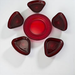 Vintage Anchor Hocking Royal Ruby relish trays arranged in a circular pattern around a coordinating red glass plate. The translucent ruby red glass glows with depth and symmetry, showcasing the sculptural triangular shapes and rich mid-century color. Ideal for holiday styling or vintage table settings.