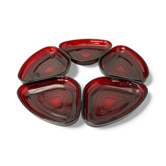 Vintage Anchor Hocking Royal Ruby relish trays arranged in a circular pattern around a coordinating red glass plate. The translucent ruby red glass glows with depth and symmetry, showcasing the sculptural triangular shapes and rich mid-century color. Ideal for holiday styling or vintage table settings.